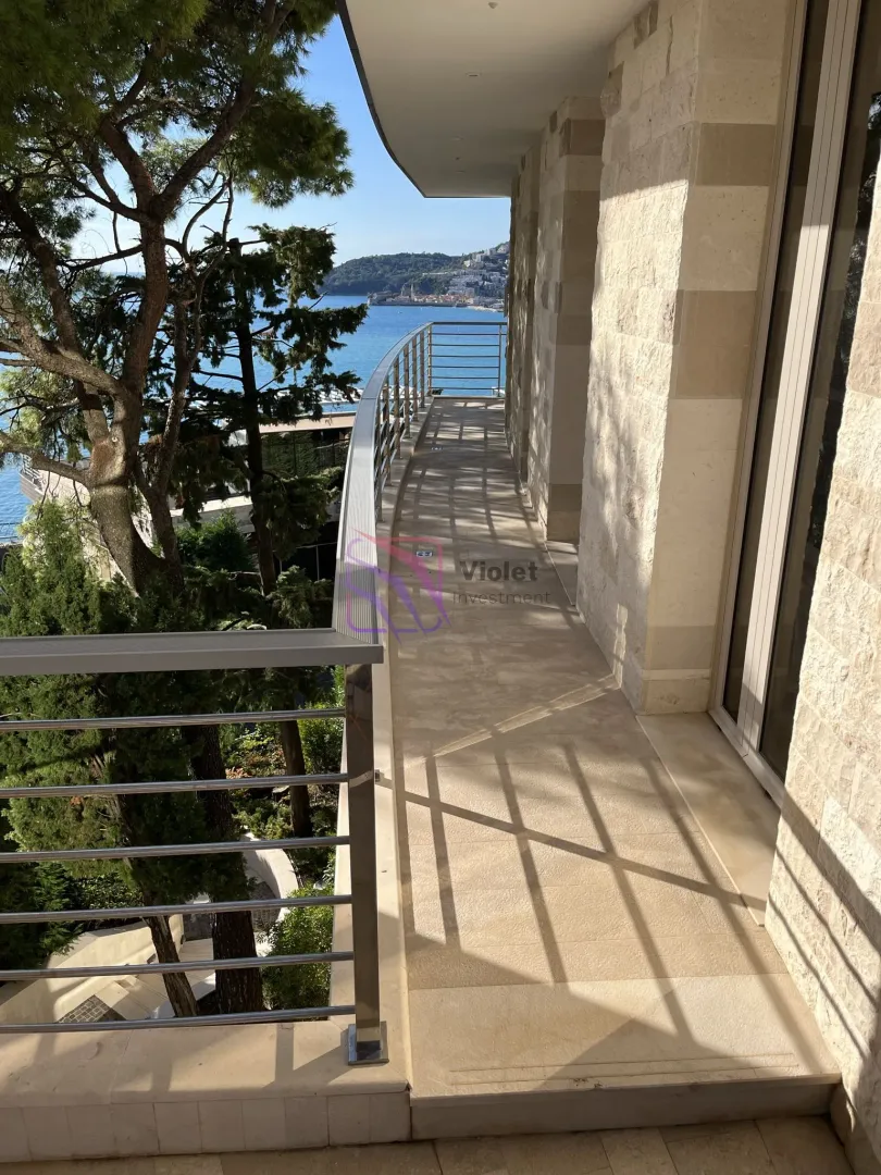Long spacious balcony with stone cladding and a metal railing, overlooking the sea.