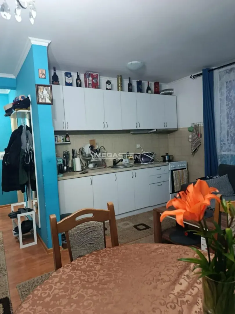 Manja kuhinja sa belim elementima i trpezarijskim stolom u prvom planu.