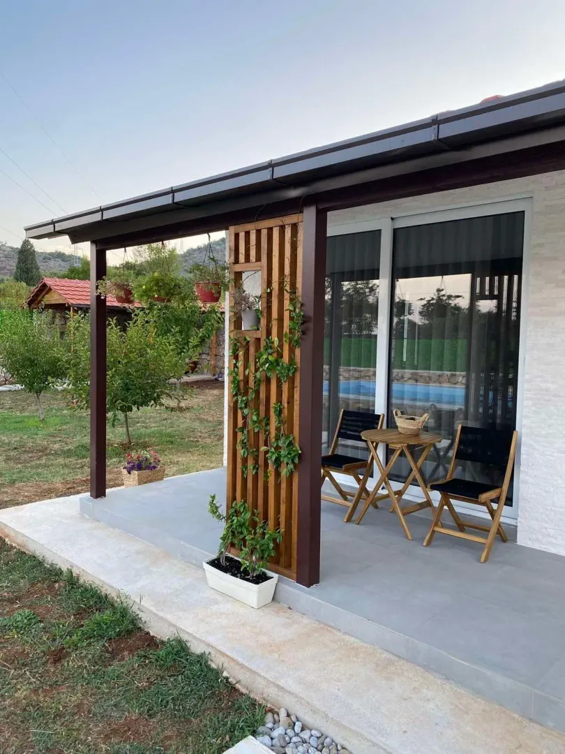 Covered terrace with a wooden table and chairs in front of the house.