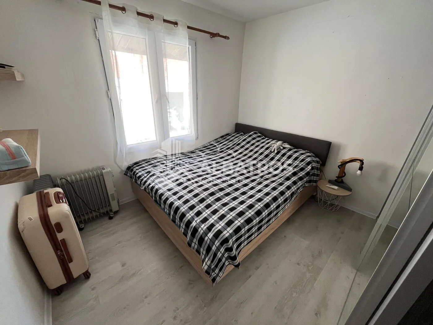 Small bedroom with a double bed, a window, and a suitcase on the floor.