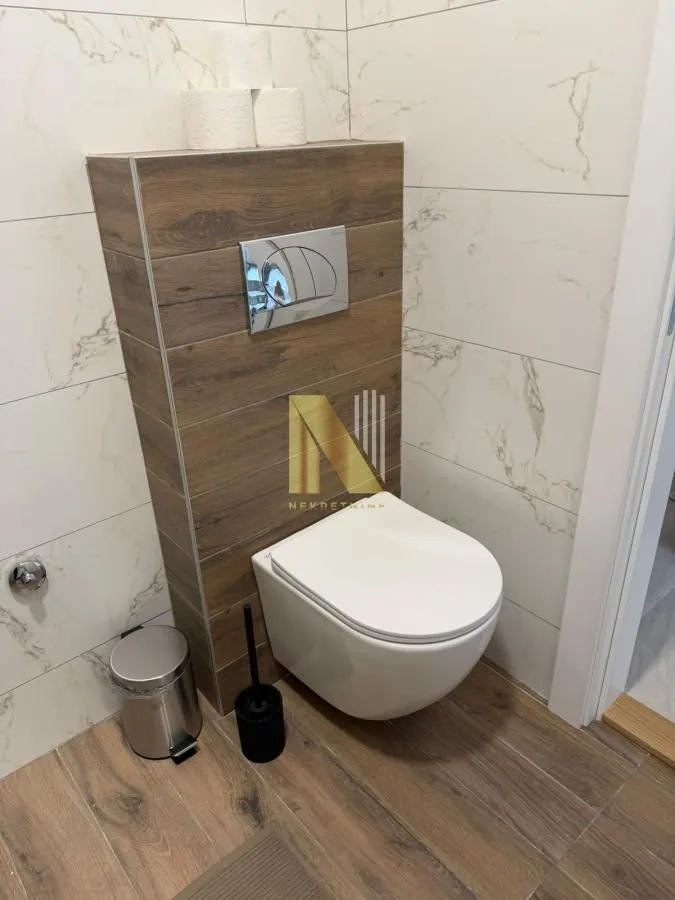 View of a modern bathroom equipped with a wall-hung toilet and wood-patterned accents.