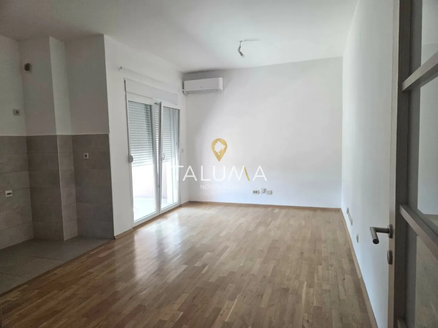Empty room with hardwood floors and balcony doors.