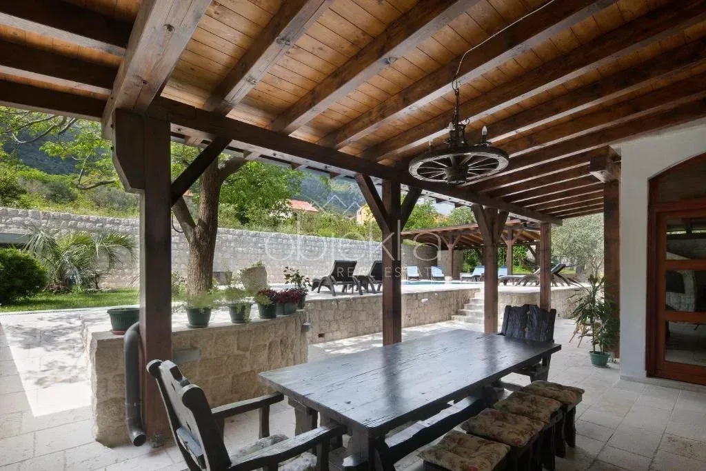 Covered terrace with wooden structure, dining table, and a view of the pool in the yard.