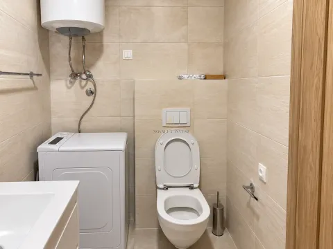 Kupatilo opremljeno toaletom, veš mašinom i bojlerom sa bež pločicama. - image 9