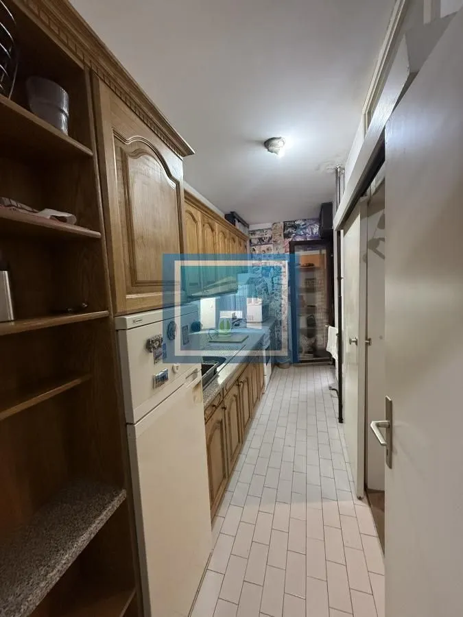 Narrow kitchen with wooden cabinets and white tiled floor.
