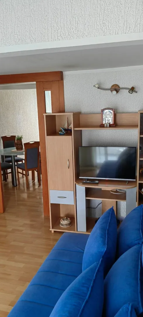 Dnevna soba sa plavom garniturom i TV komodom, sa pogledom na trpezariju.