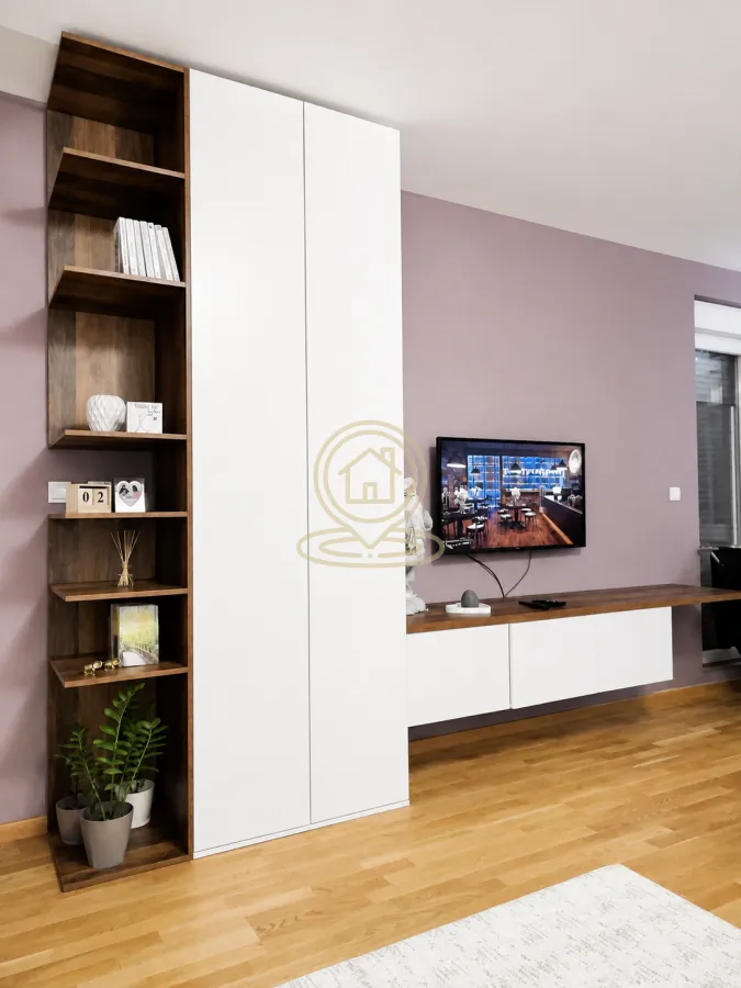 Dnevni boravak sa modernim zidnim nameštajem, policama i televizorom.