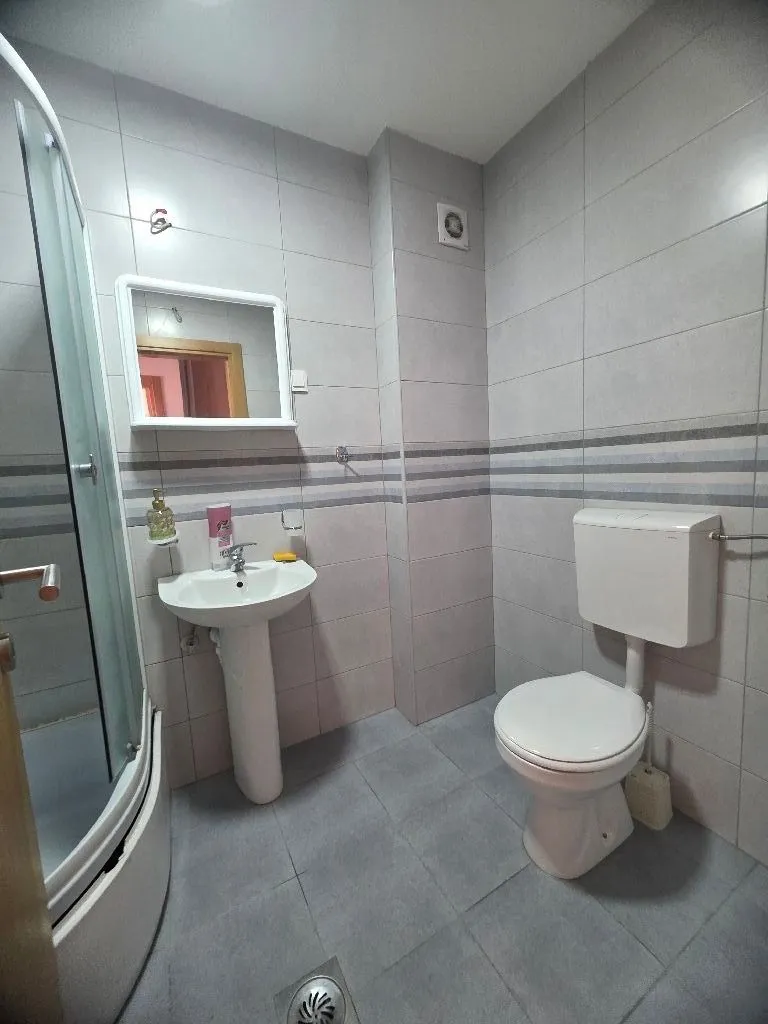 Manje kupatilo sa tuš kabinom, umivaonikom i WC šoljom obloženo svijetlim pločicama.