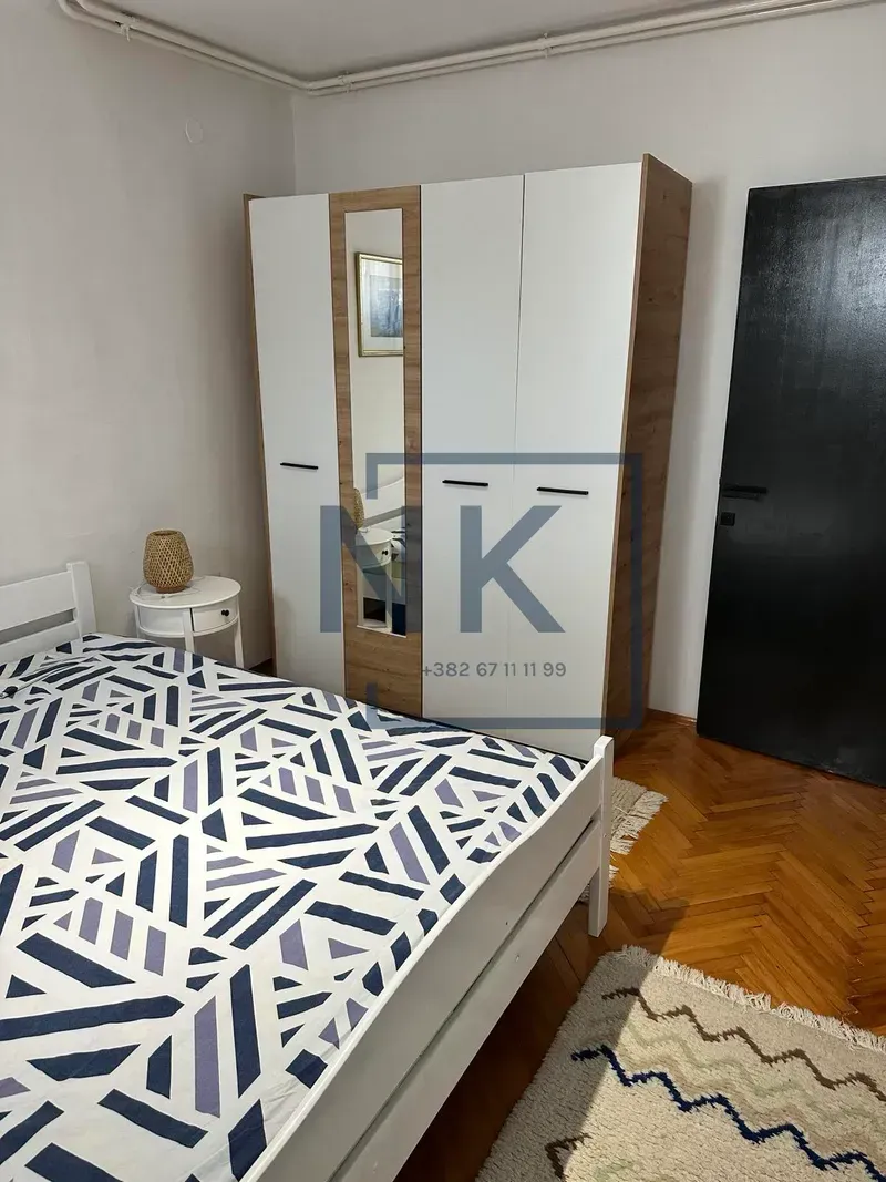 Furnished bedroom with a double bed, white wardrobe, and wooden flooring.