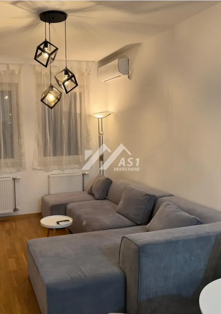 Ugaona garnitura u dnevnoj sobi sa modernim lusterom i klima uređajem.