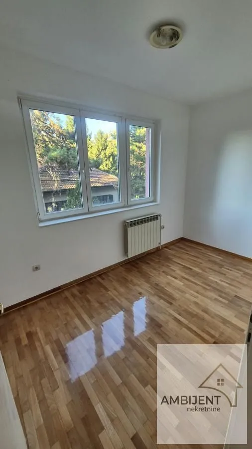 Prazna soba sa parketom i prozorom koji gleda na zelenilo.