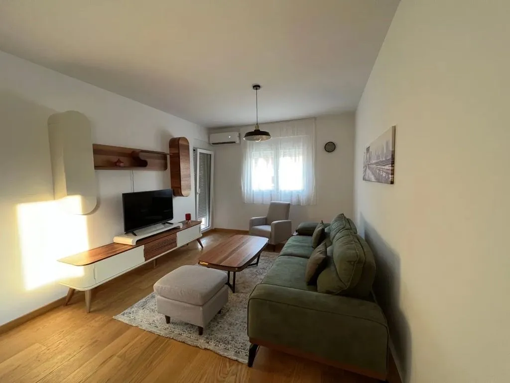 Living room with a sofa, TV, and wooden flooring.