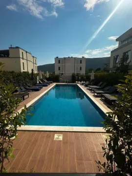 Outdoor swimming pool with sun loungers surrounded by buildings and greenery. - image 6
