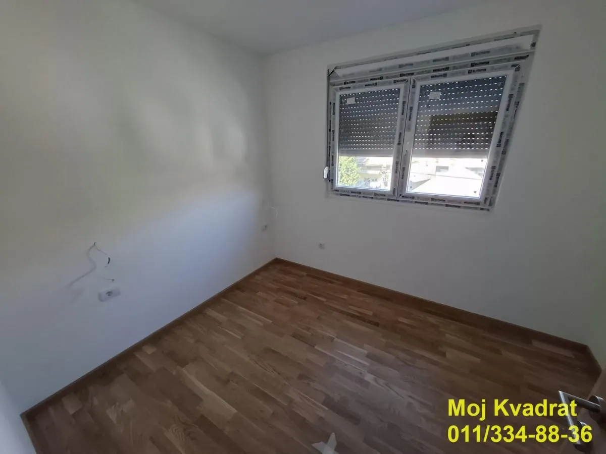 Prazna soba sa laminatom i belim zidovima.