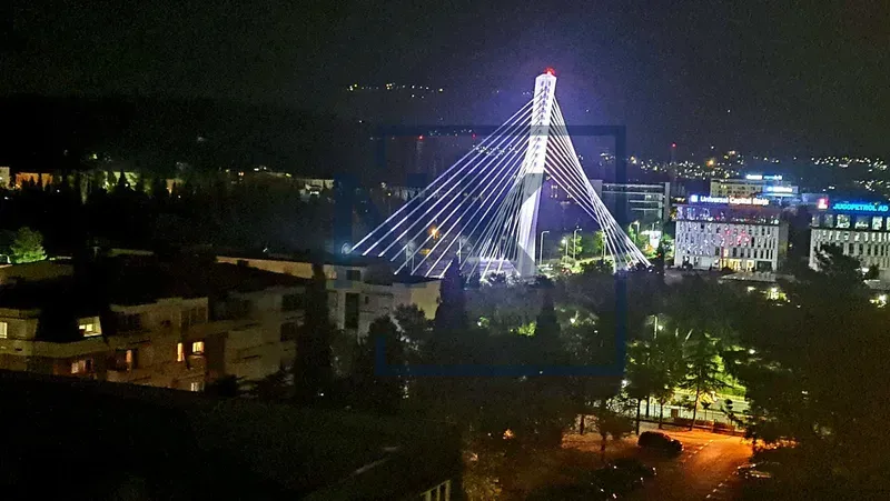 Noćni pogled sa prozora na osvijetljeni most i grad.