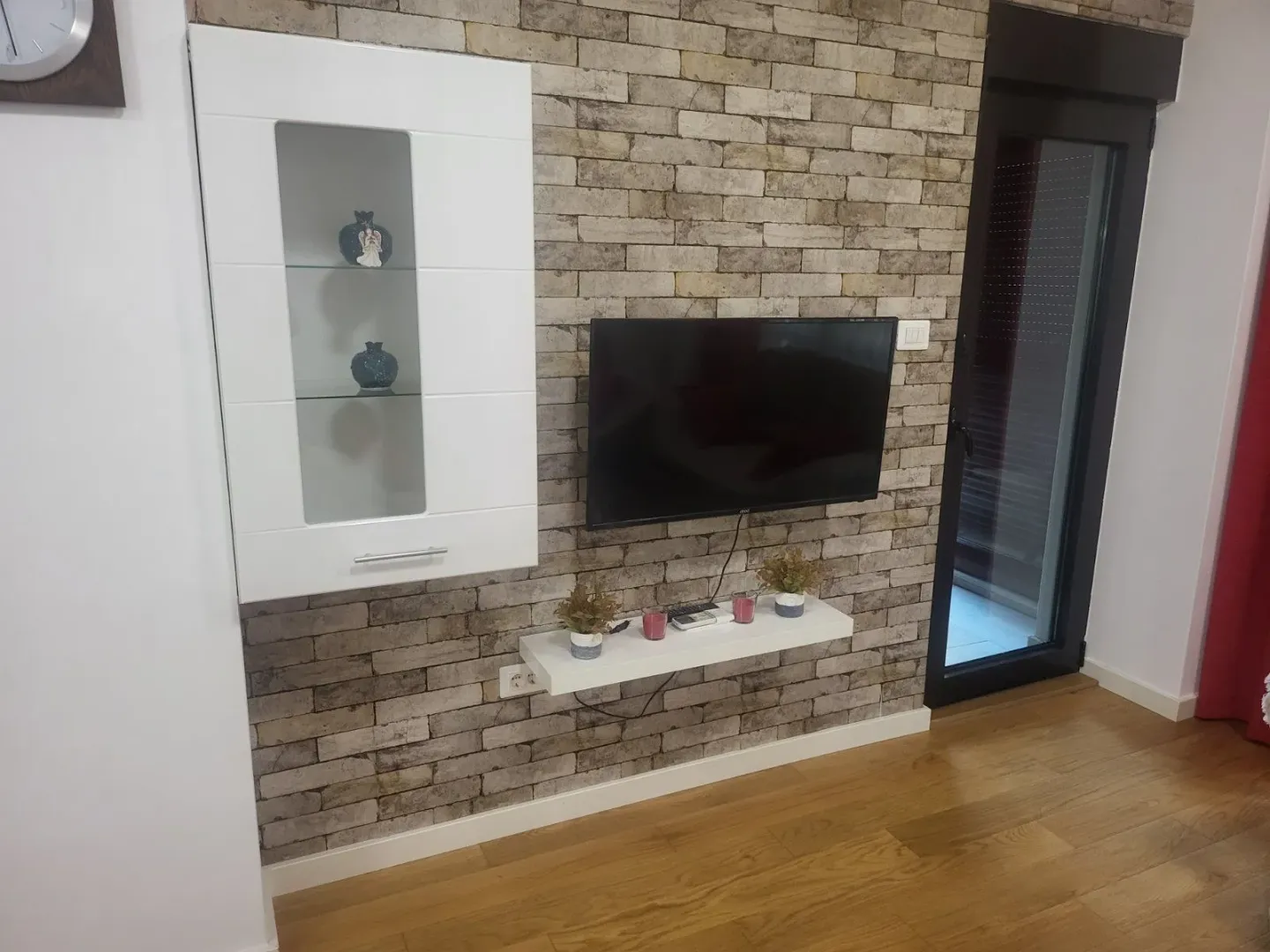 A wall with decorative brickwork, a mounted TV, and a floating shelf in a living room.