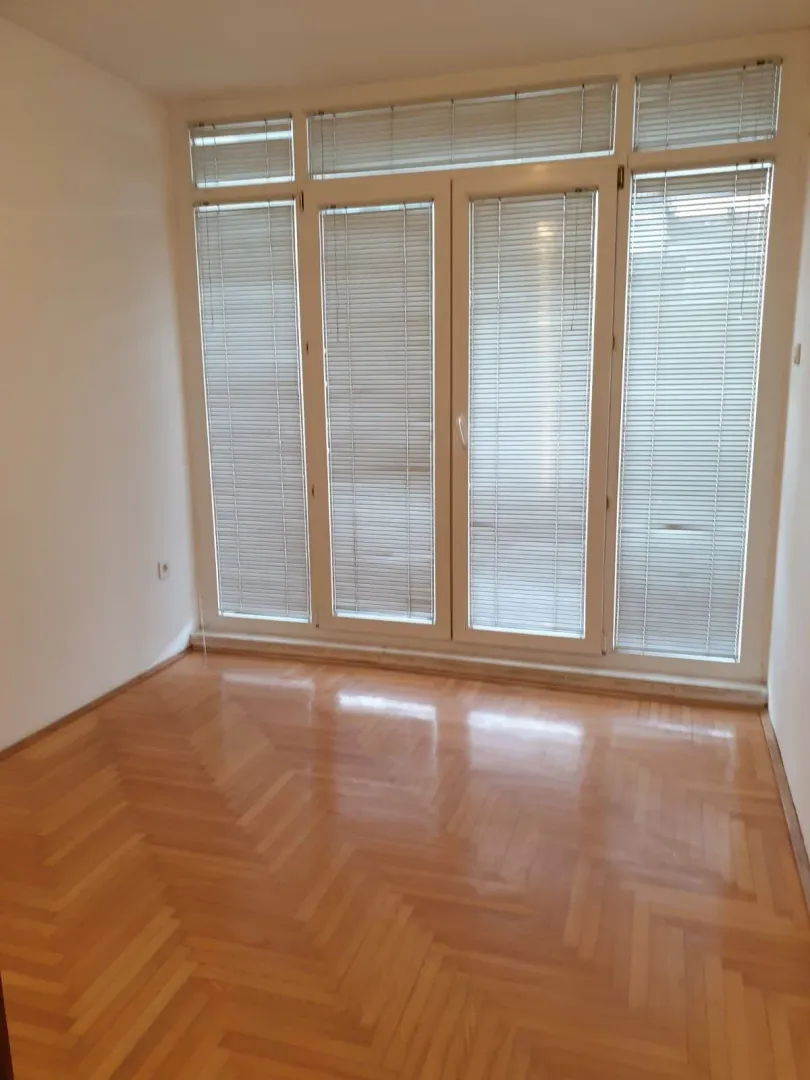Bright empty room featuring parquet flooring and large balcony doors with blinds.