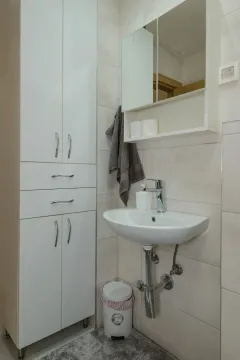 Svijetlo kupatilo sa bijelim ormarićem i umivaonikom. - image 11