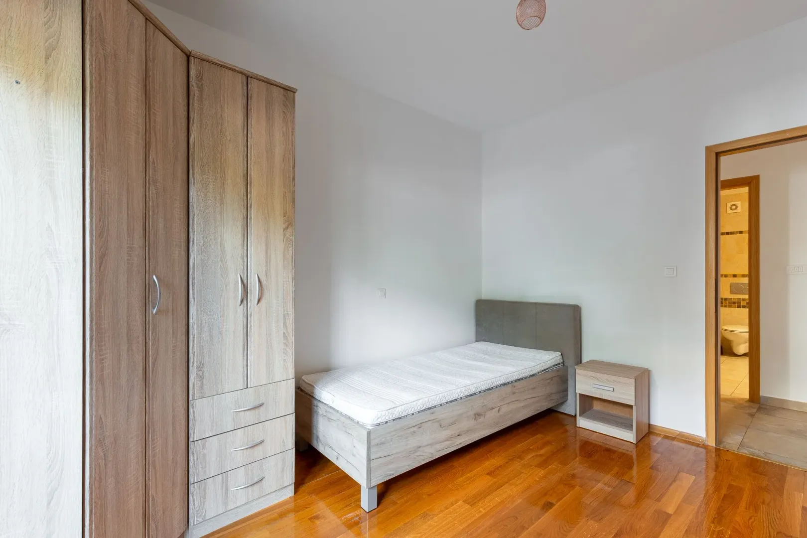 Bedroom with a single bed, wooden wardrobe, and a nightstand.