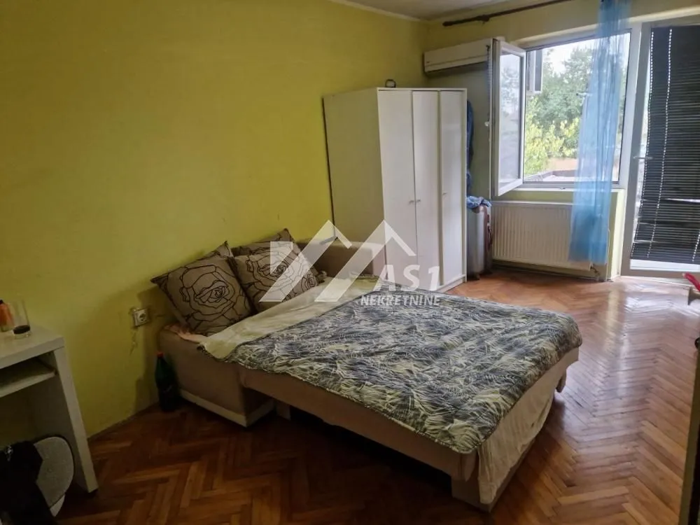 Nameštena spavaća soba sa krevetom, ormarom i izlazom na terasu.