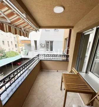 Natkrivena terasa sa drvenim stolom i pogledom na okolne zgrade. - image 12