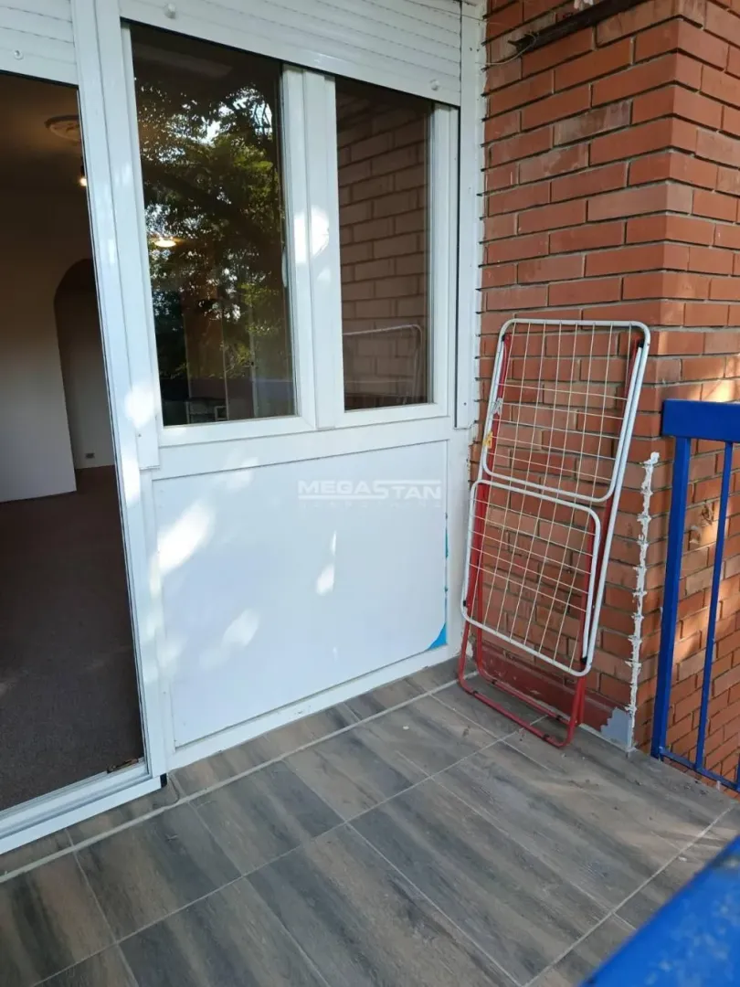 Pogled na popločanu terasu sa balkonskim vratima i sklopivom sušilicom za veš.