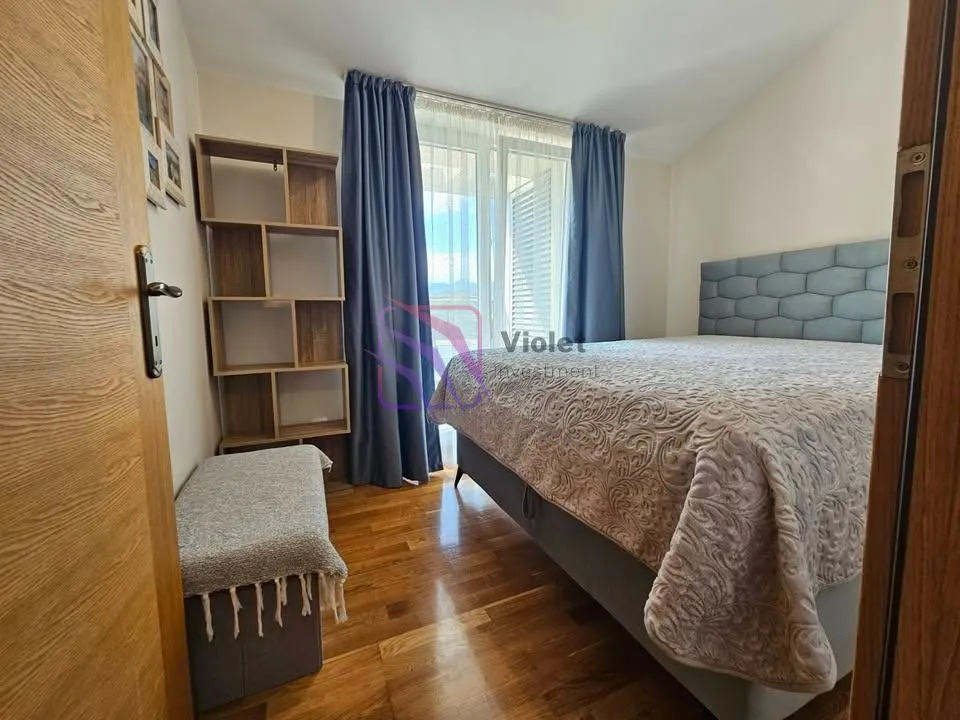 Furnished bedroom with a double bed, wooden shelving unit, and balcony doors.