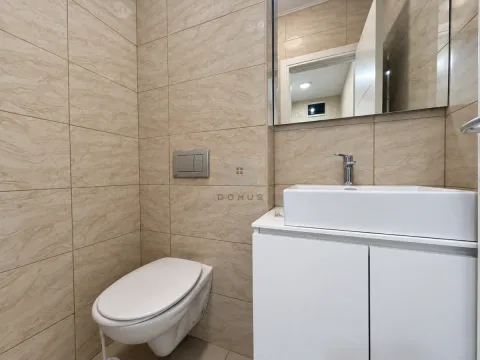 Manje kupatilo obloženo bež pločicama sa ugradnim wc šoljom i bijelim umivaonikom. - image 12