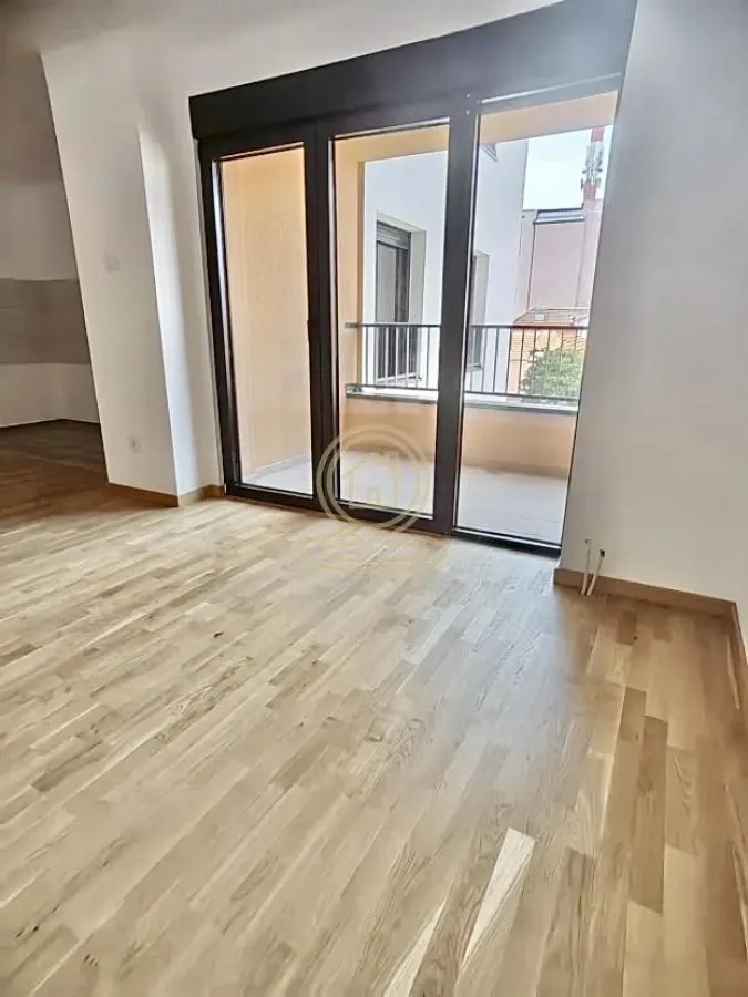Prazna soba sa drvenim parketom i izlazom na terasu.