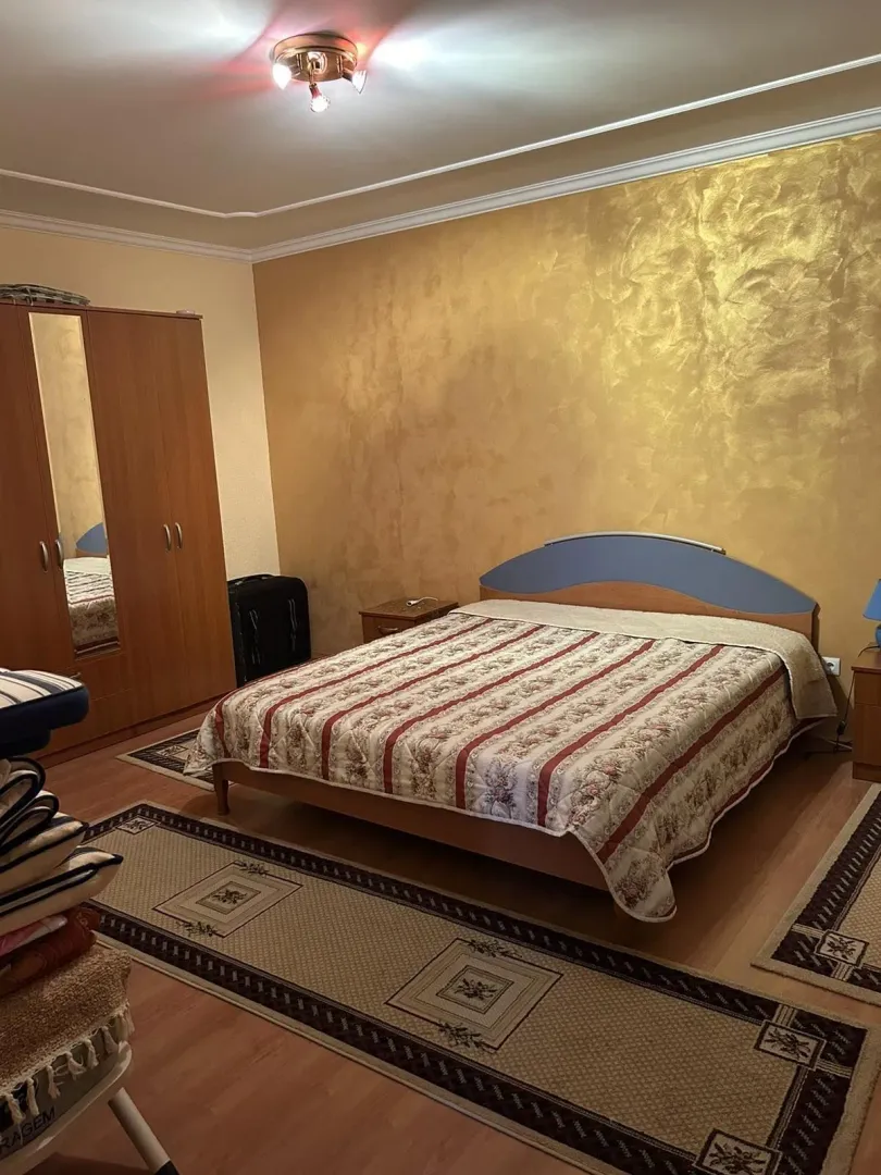 A bedroom featuring a double bed, a wooden wardrobe, and a gold accent wall.