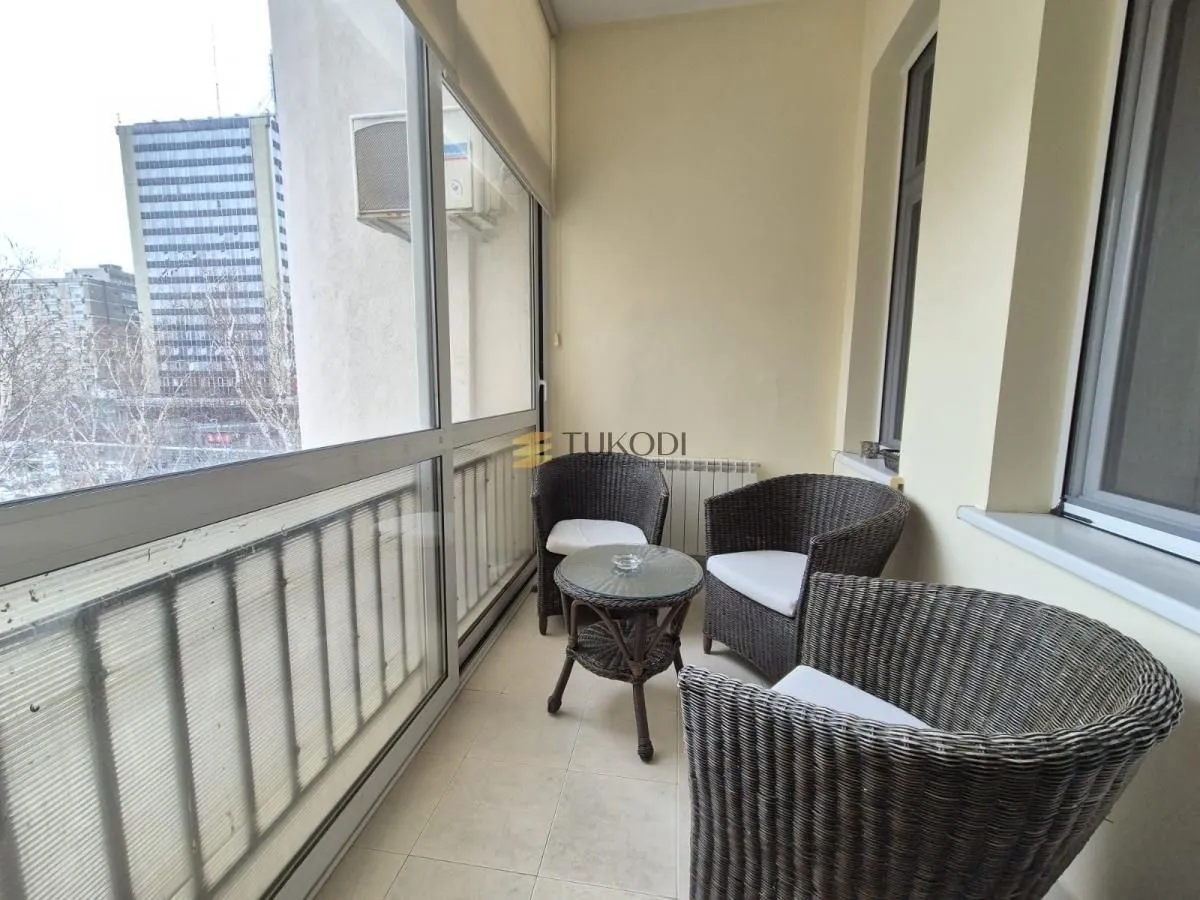 Zastakljeni balkon sa garniturom za sedenje i pogledom na grad.