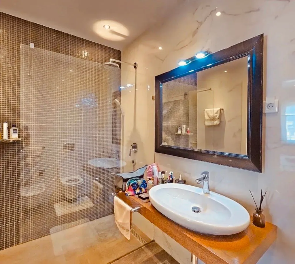 Modern bathroom with a sink on a wooden countertop, a large mirror, and a walk-in shower.