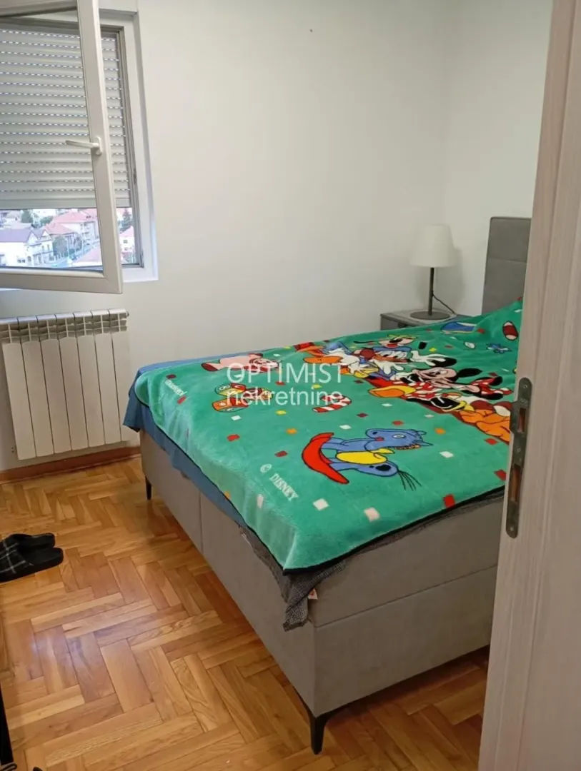 Spavaća soba sa krevetom, noćnim stočićem i prozorom.