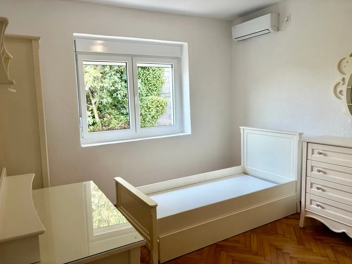 Bright bedroom with a white bed, dresser, and wardrobe.