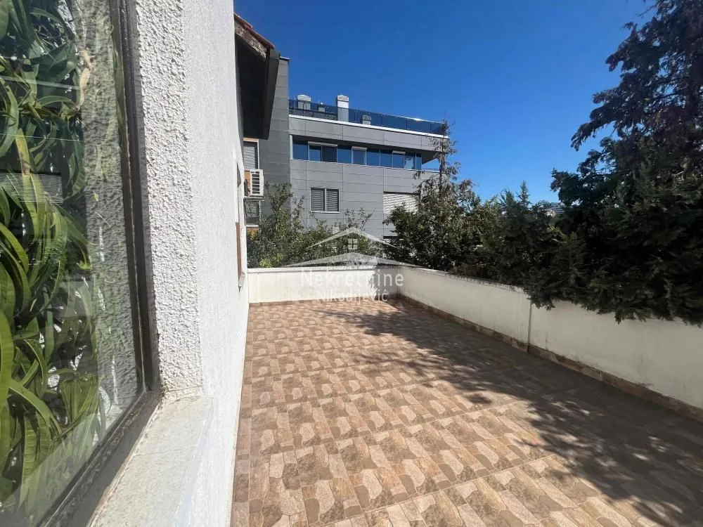 Spacious tiled terrace with a view of the surrounding greenery and buildings.