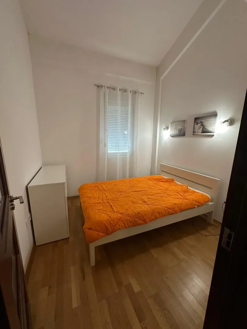 Svijetla spavaća soba sa bijelim krevetom i narandžastom posteljinom.