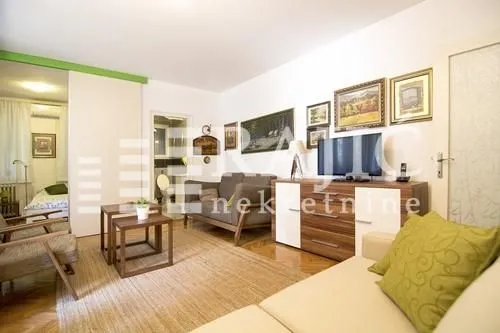 Furnished living room with a sofa, TV, and a view towards the bedroom hallway.
