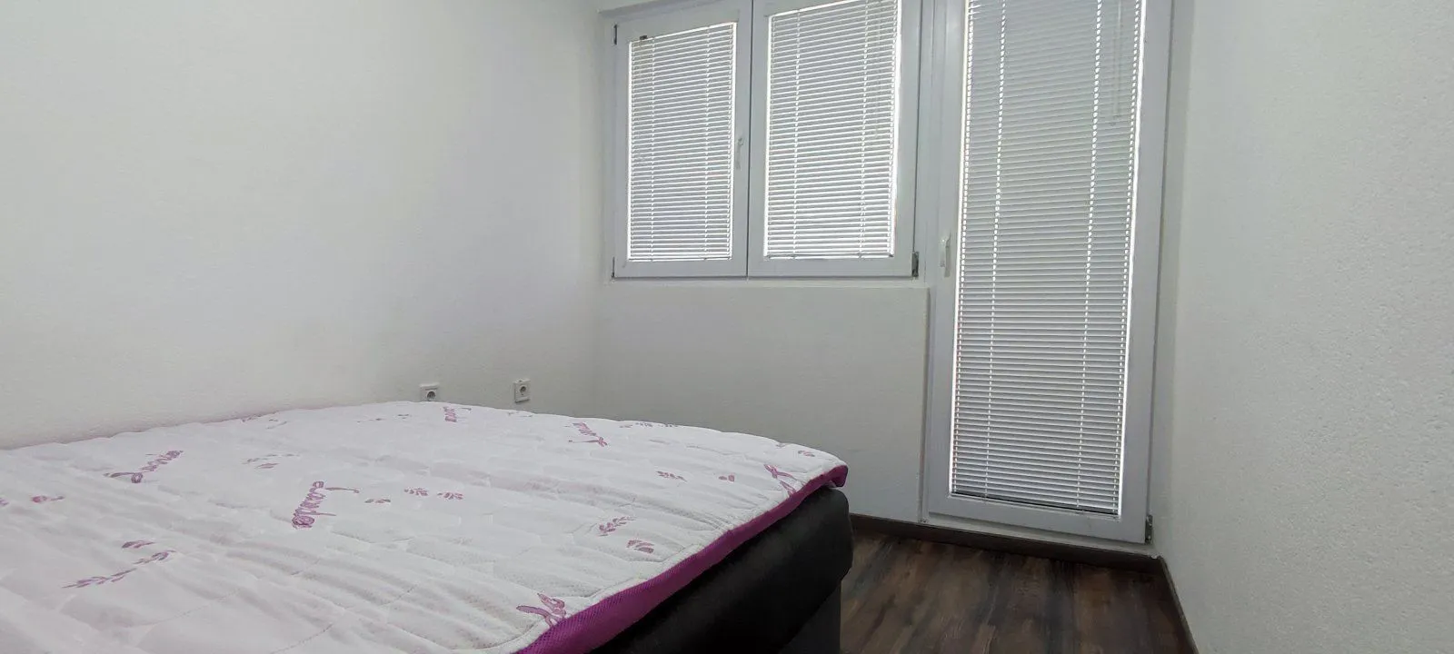 A simple bedroom with a double bed and windows with blinds.