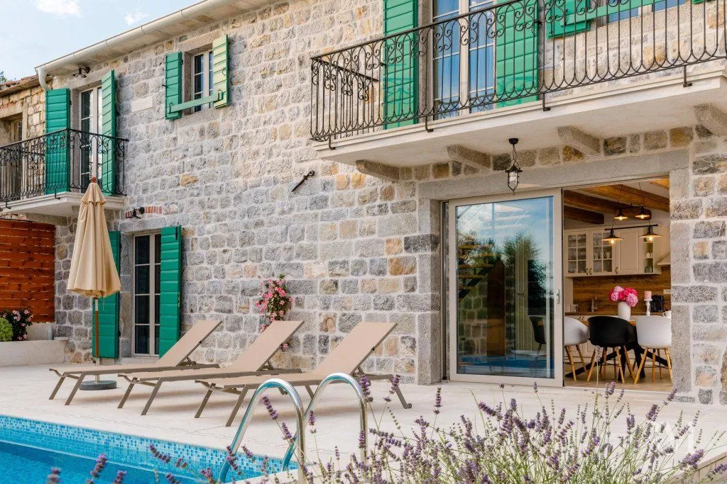 Exterior of a stone house with a swimming pool and sun loungers.