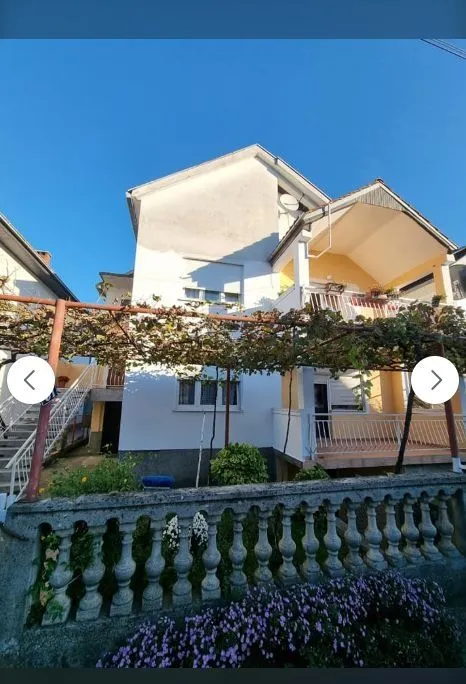Vanjski izgled dvospratne kuće sa dvorištem i ogradom.