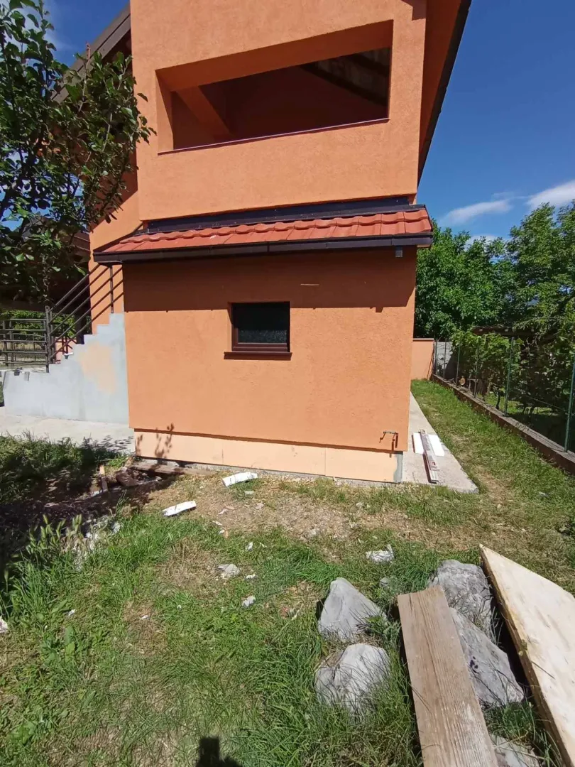 Pogled na spoljašnjost kuće narandžaste fasade sa dvorištem.