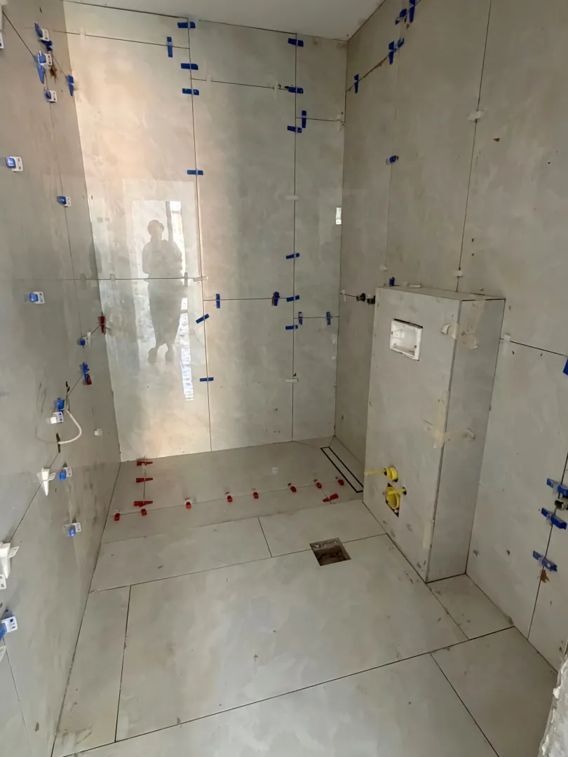Bathroom undergoing tiling work with installed tiles and leveling spacers.