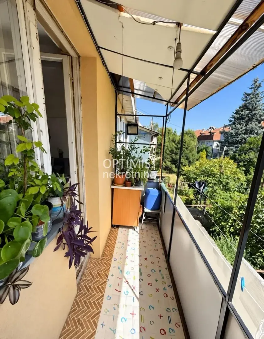 Natkriveni balkon sa saksijama sa cvećem i pogledom na zelenilo.