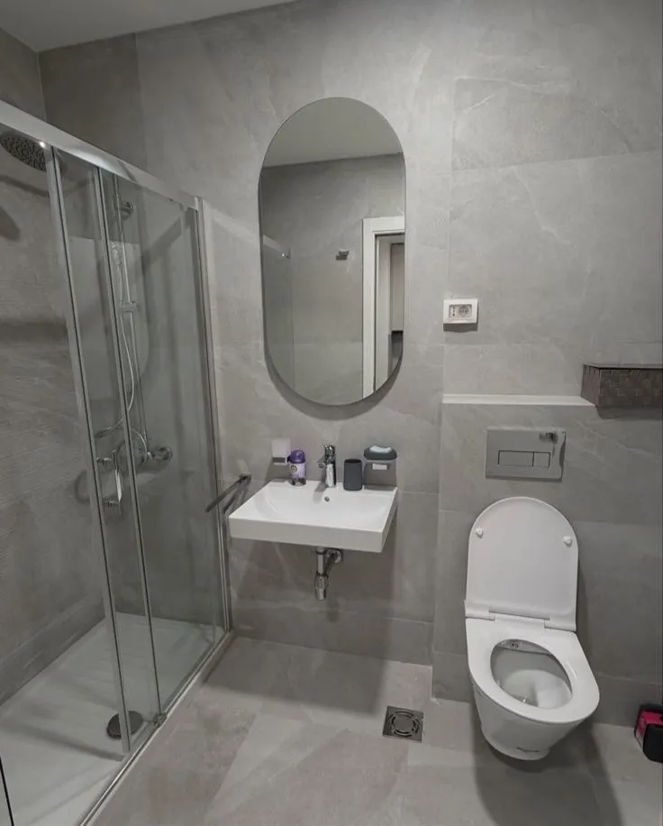 Moderne kupatilo sa tuš kabinom, umivaonikom i toaletom u sivim tonovima pločica.