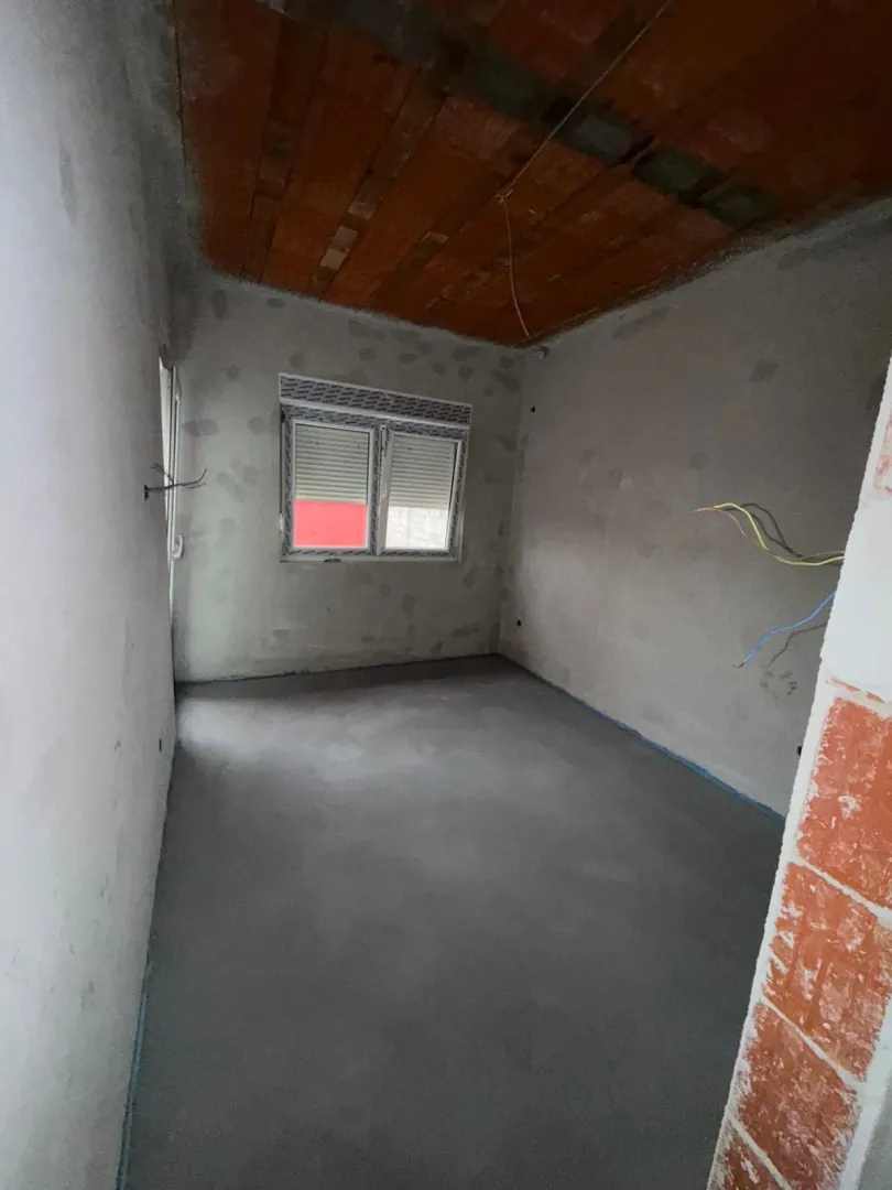 Nedovršena prostorija u izgradnji sa betonskim podom i malterisanim zidovima.
