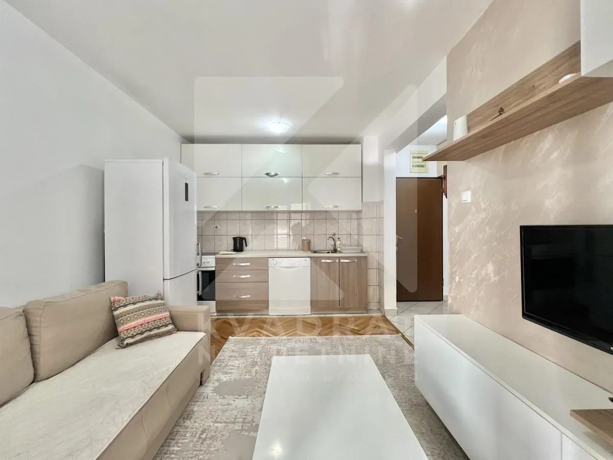 Living room with sofa, TV and kitchen in the background.
