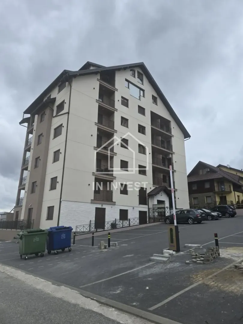 Pogled na spoljašnjost stambene zgrade sa parkingom i rampom.