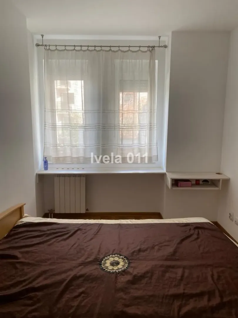 Spavaća soba sa bračnim krevetom i prozorom sa zavesama.