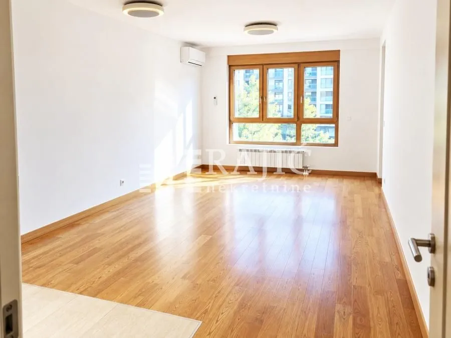 Empty living room with parquet flooring and a large window.