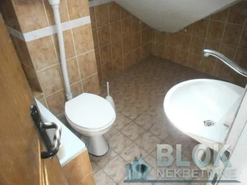 Small tiled bathroom with a toilet, washbasin, and sloping ceiling. - image 8